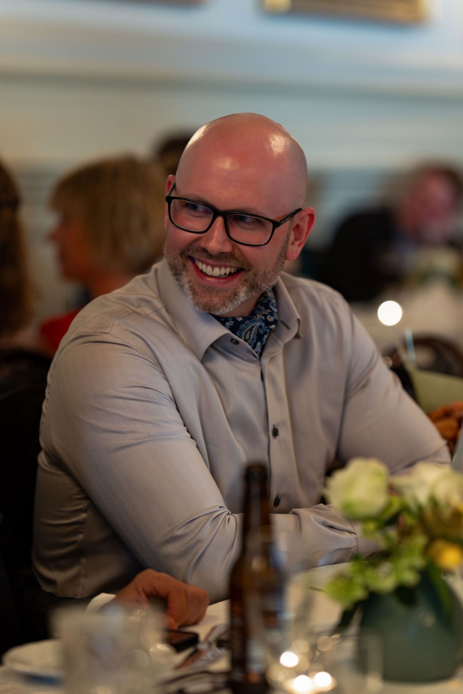 Guest in light gray suit and bow tie smiling during formal dinner.