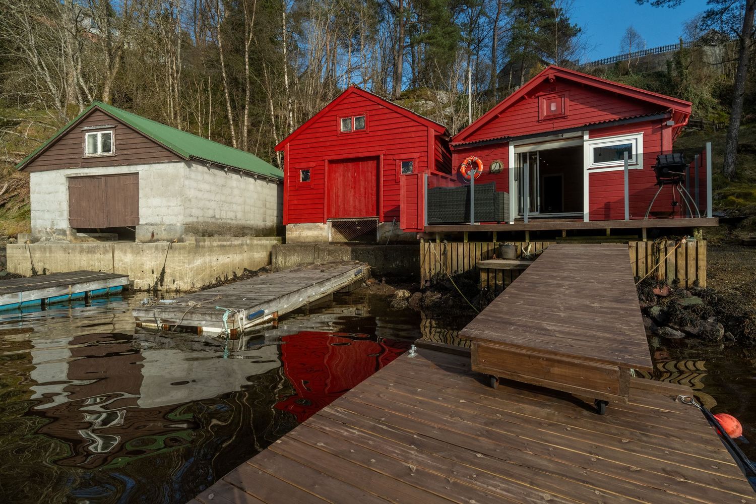 Bright red waterfront cabins with wooden dock and gray building beside tranquil water.
