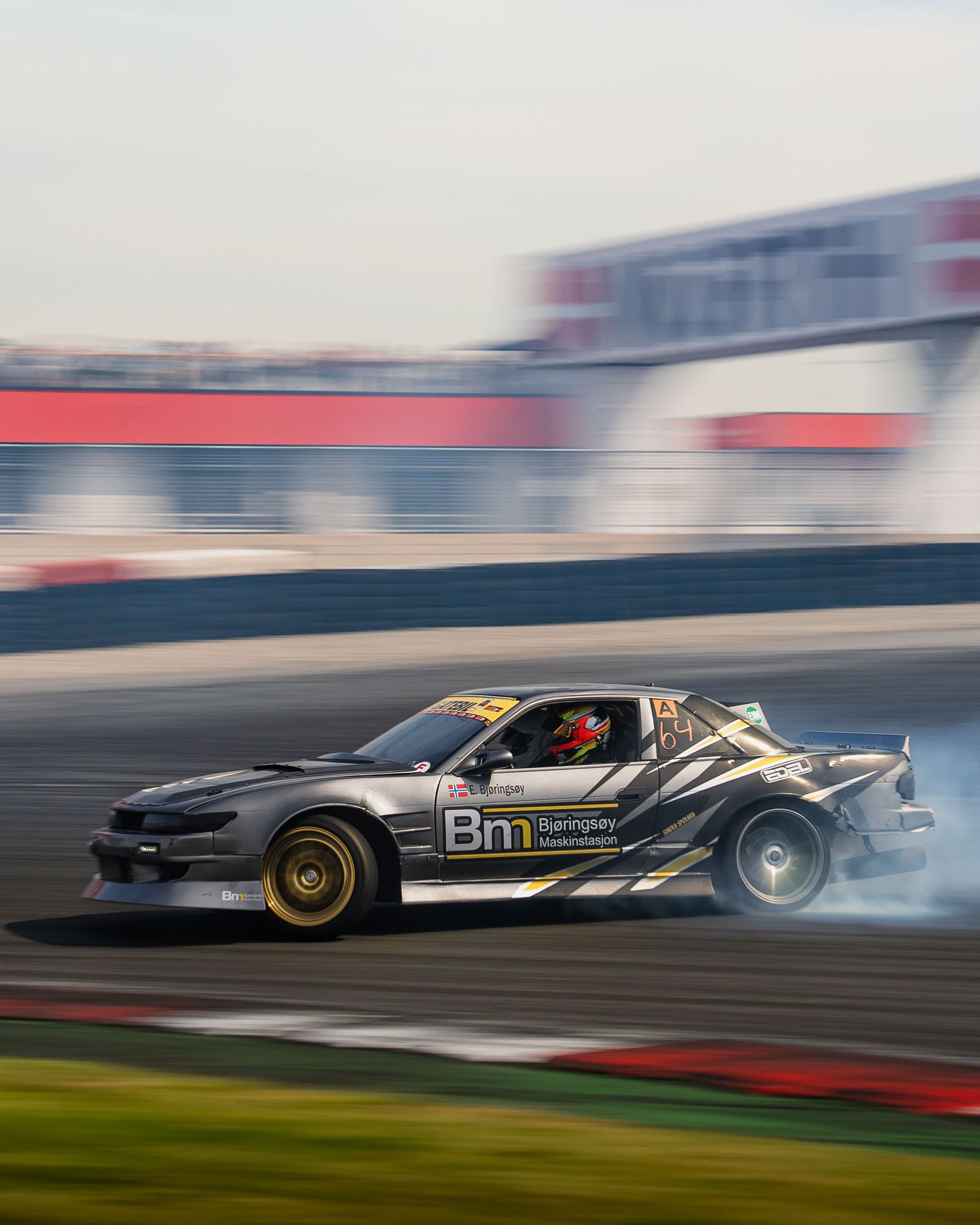 Drifting race cars create tire smoke while competing on a track during a professional motorsport competition.