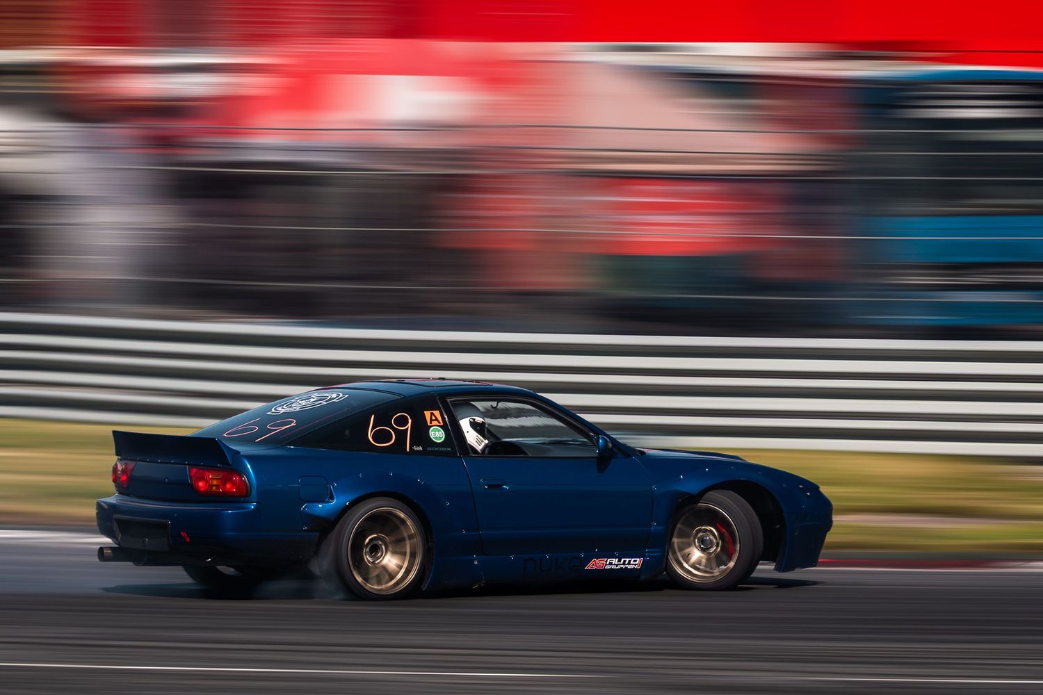 Race cars speed along a racetrack with motion blur against vibrant red and blue background elements.