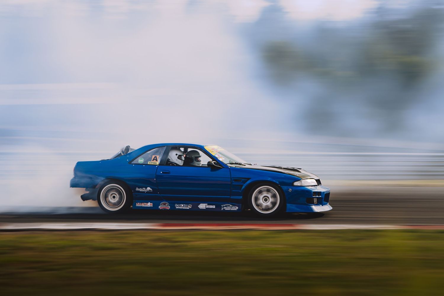 Blue drift car racing sideways on a track with motion blur creating a dramatic action shot.