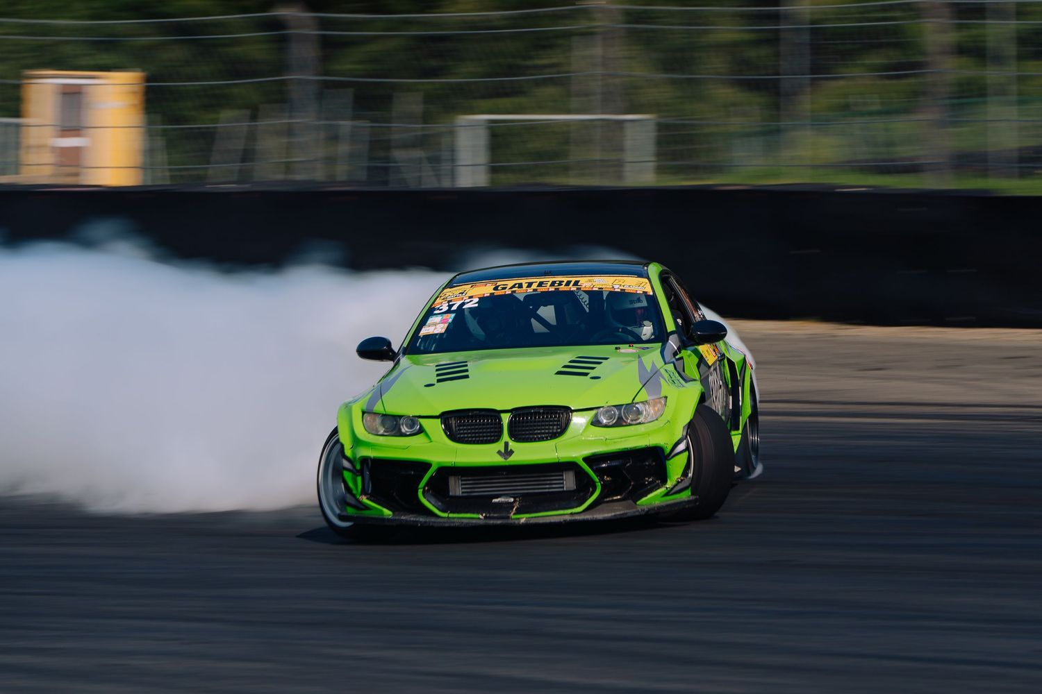 Bright green BMW sports car drifting on a race track with smoke trailing from the rear tires.