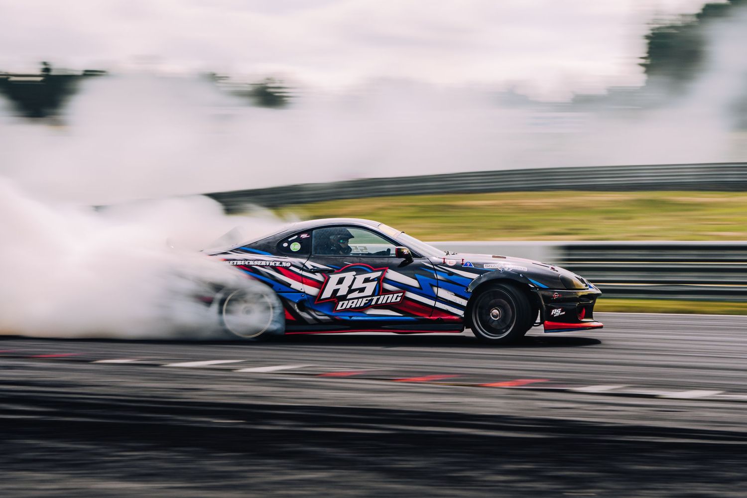 Racing car drifts around a track creating smoke while competing in a motorsport event.