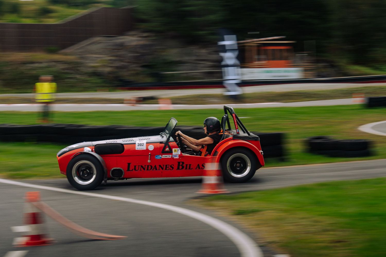 A red vintage sports car navigates through a winding road course during a racing event.