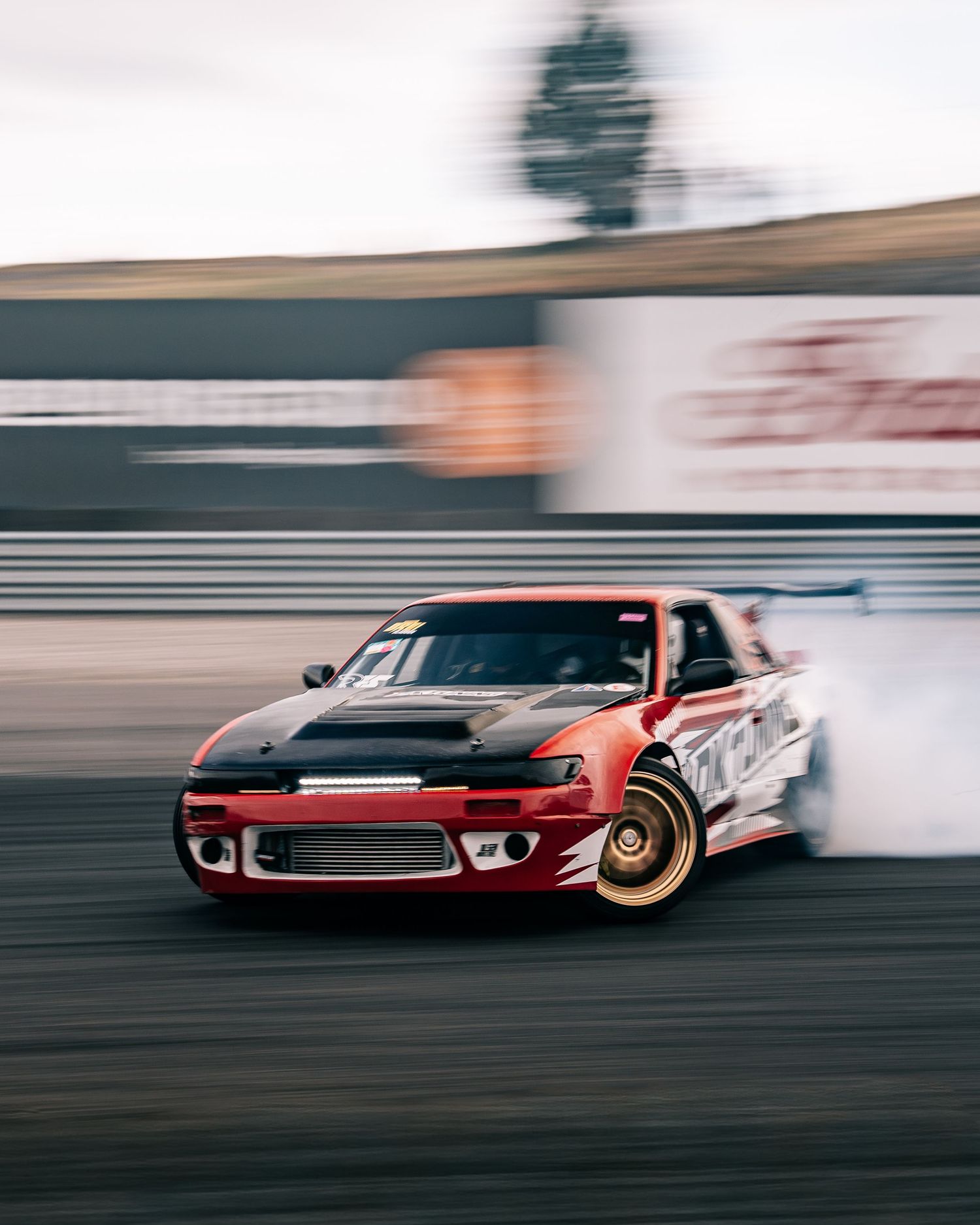 Red vintage muscle car drifting on race track with motion blur effect showing speed and performance.
