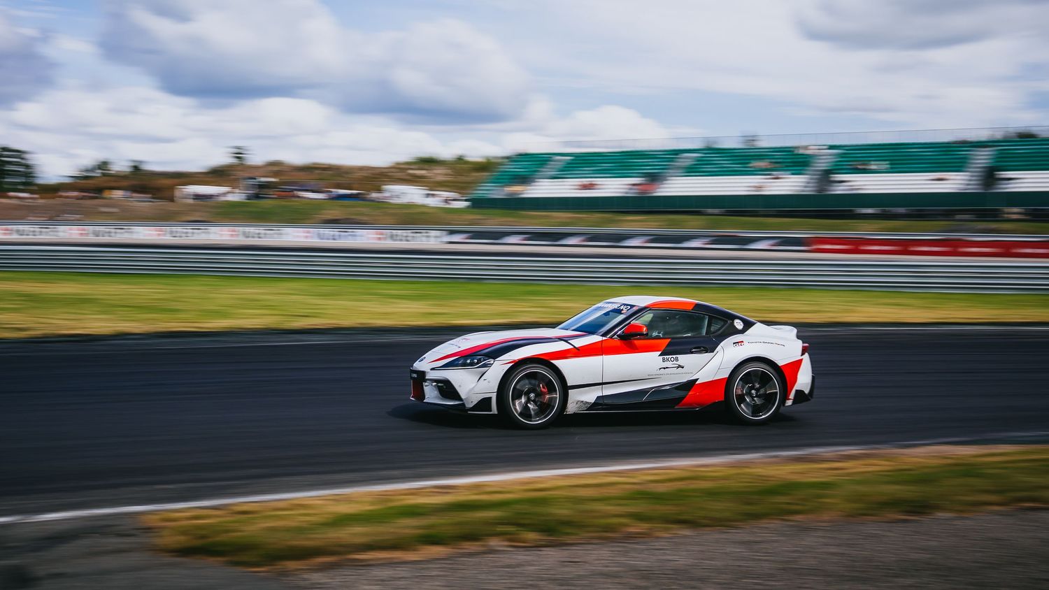 A white and red Toyota Supra race car speeds around a racetrack corner with motion blur effect.