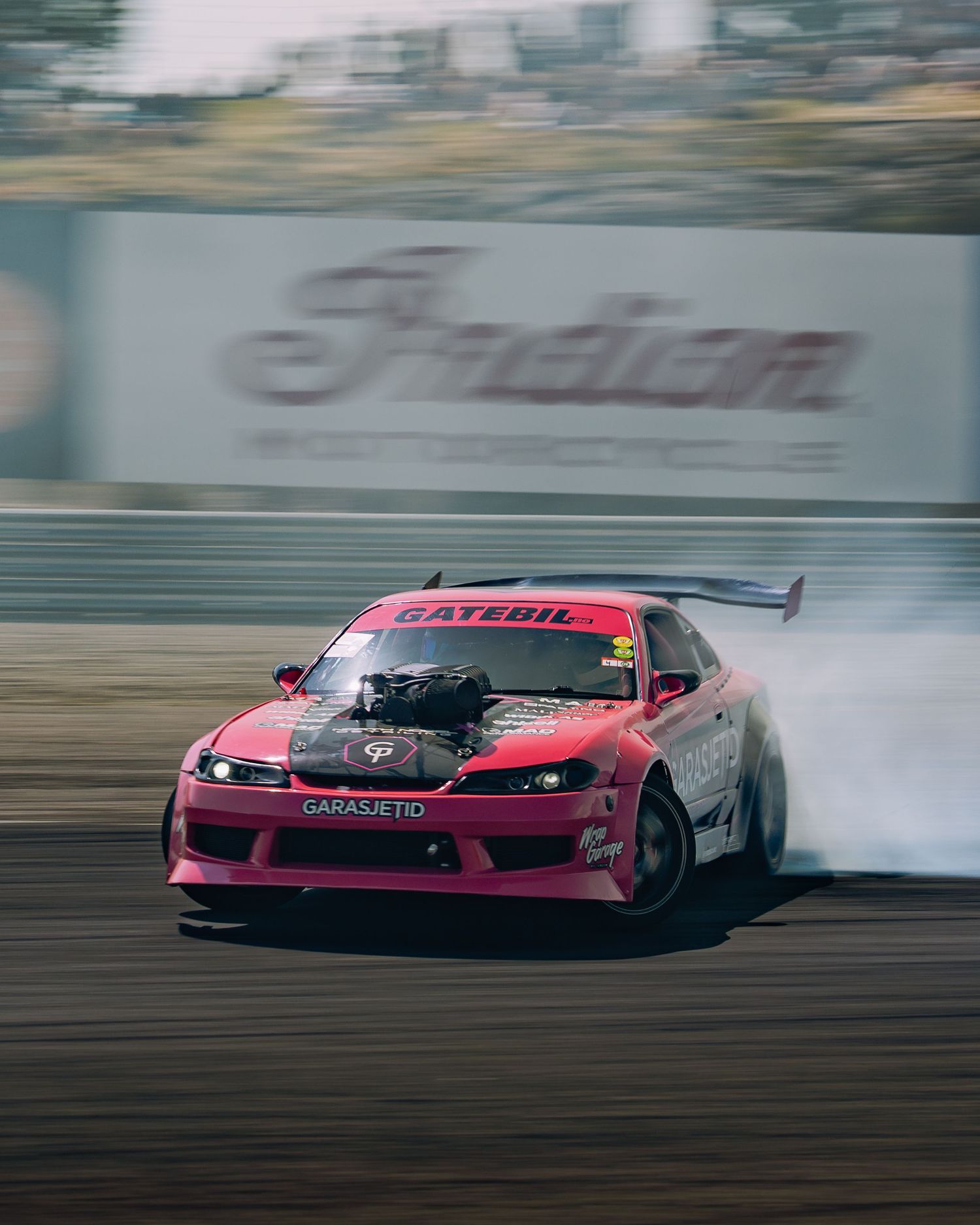 Red drift car performs a high-speed slide on a racetrack creating dramatic smoke from its tires.