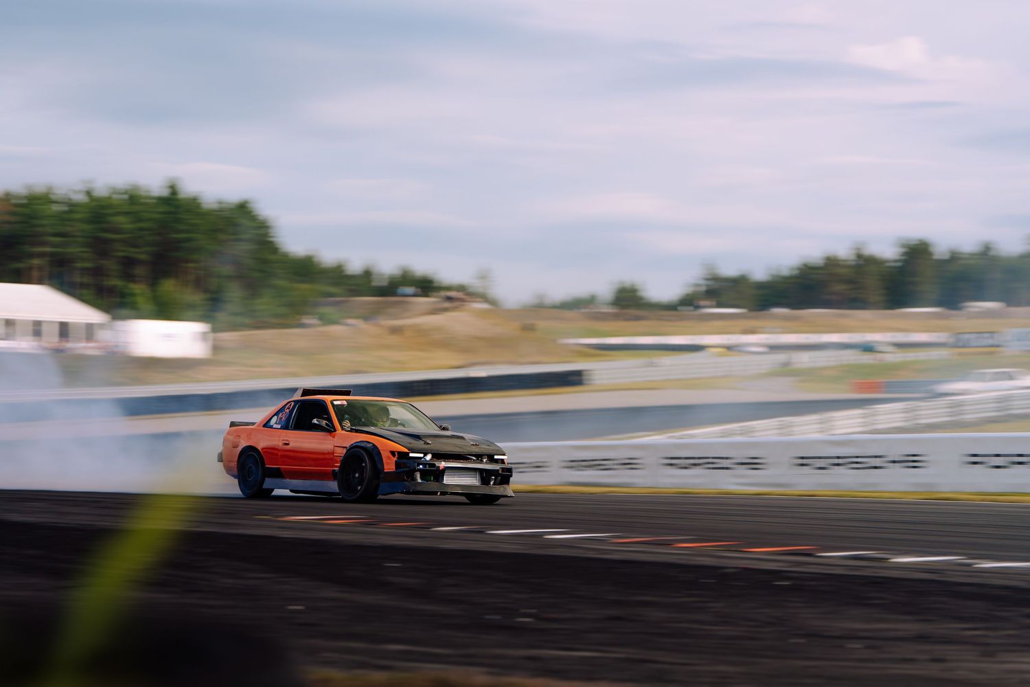 Multiple drift cars sliding sideways on a race track creating smoke during a competitive drift event.