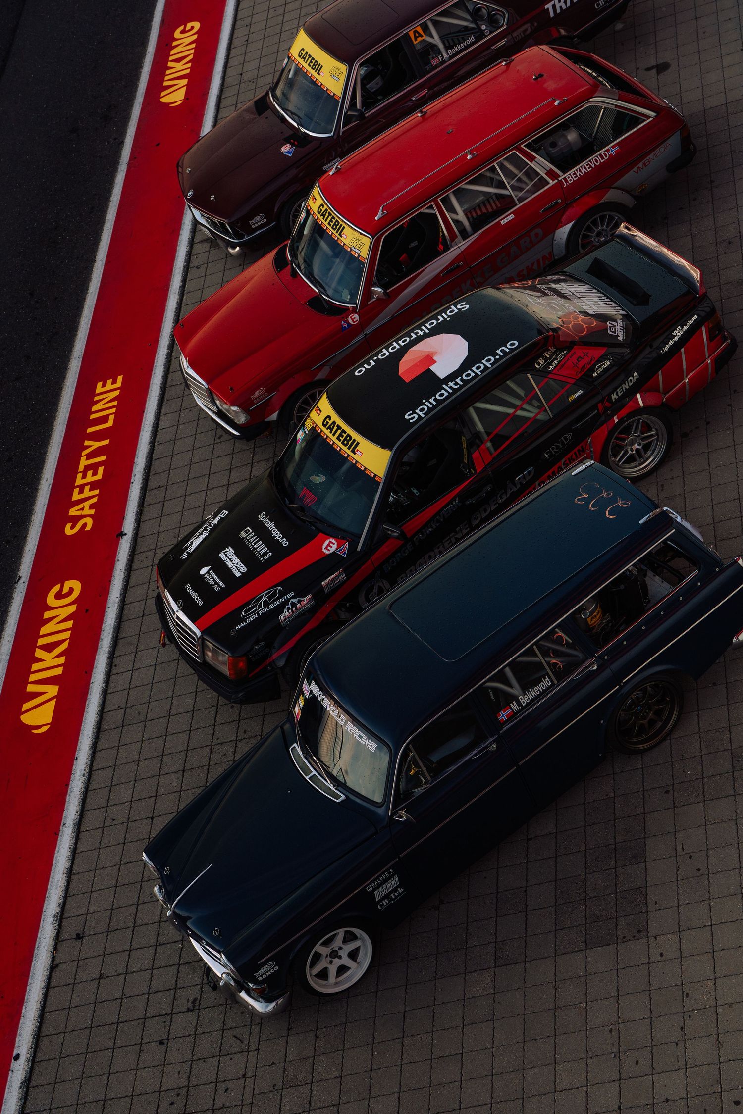 Aerial view of classic red and black vintage cars parked diagonally in a row on a dark paved surface.