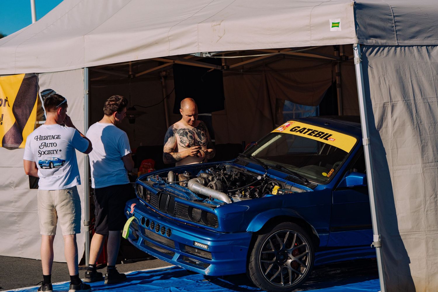 A blue BMW M4 is being detailed and polished at an auto show or car event.