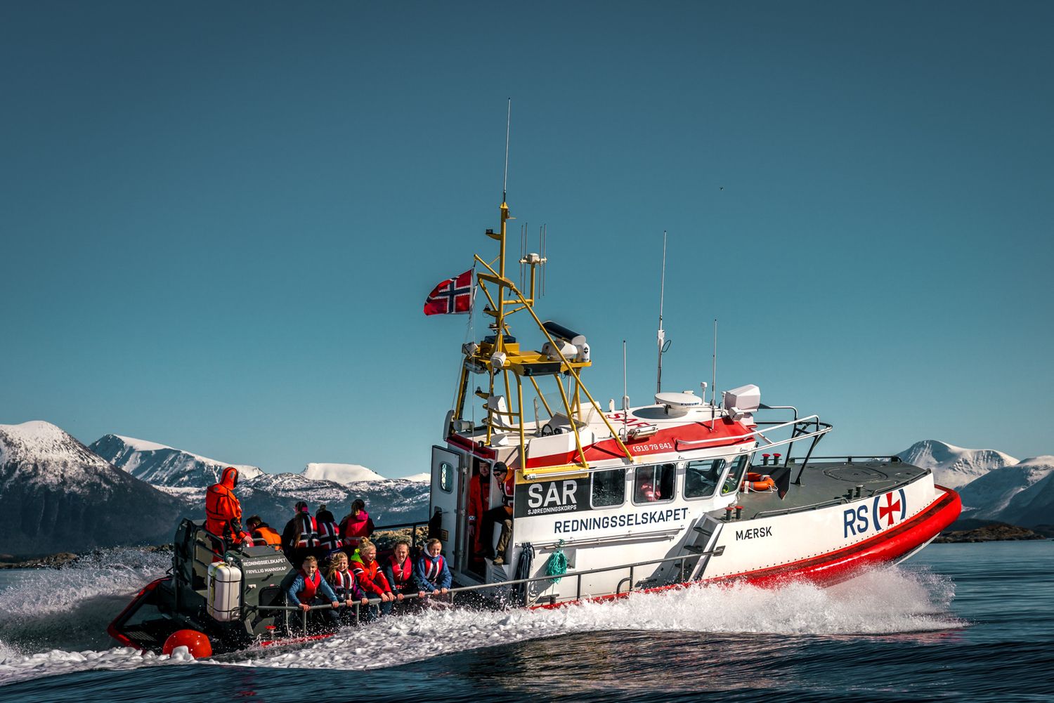 Norwegian rescue vessel conducting operations in cold waters with mountainous backdrop.