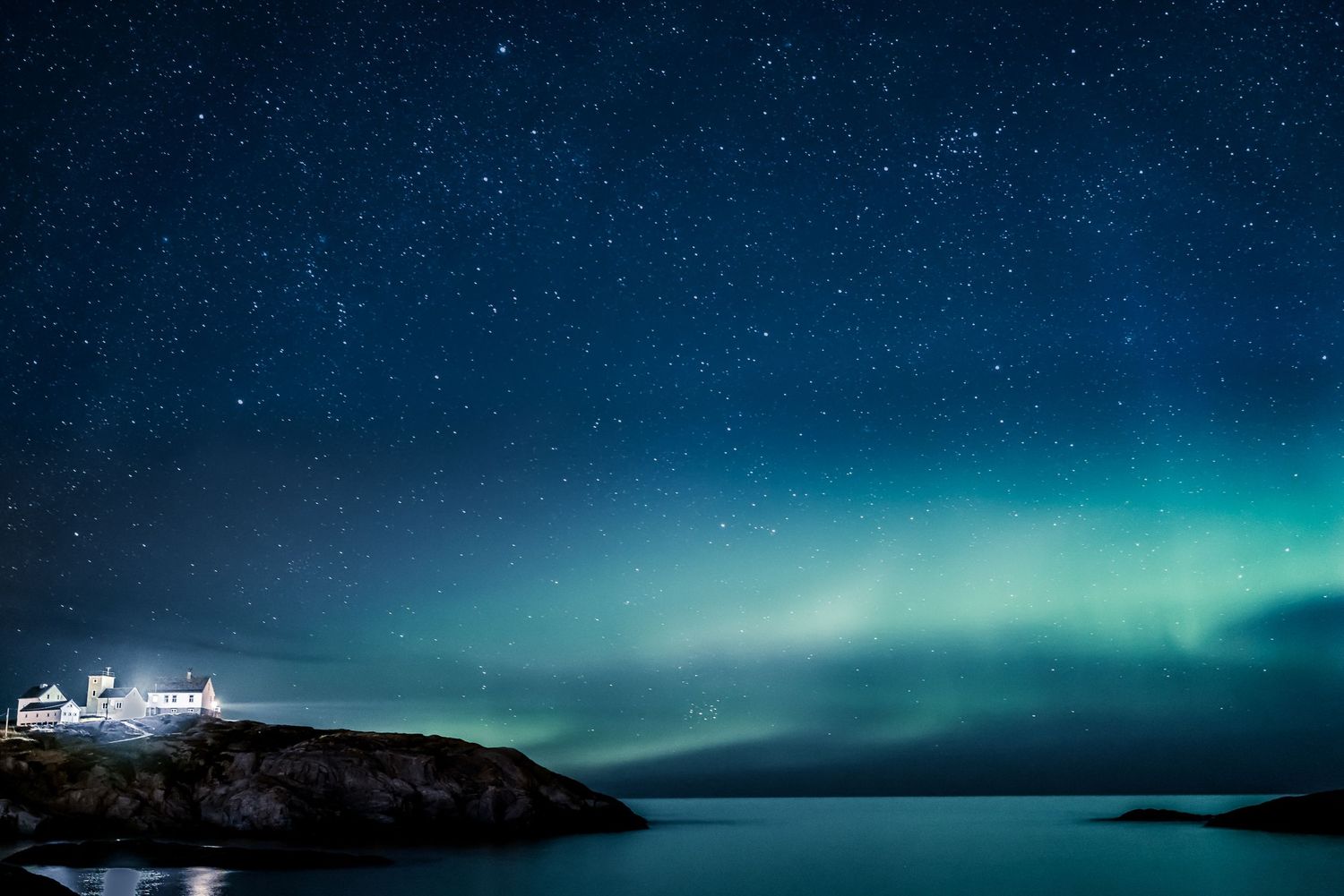 Northern lights glow green over a coastal lighthouse and dark waters.