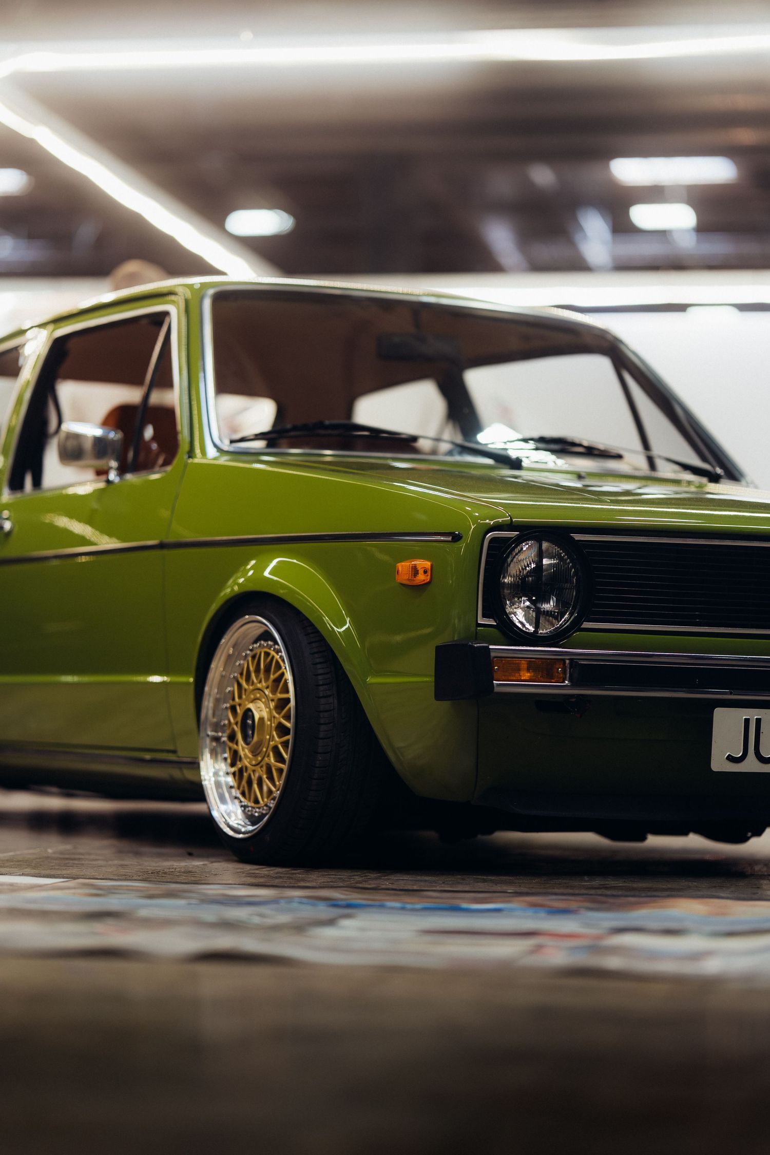 Lime green classic car with custom gold wheels photographed from low angle in indoor setting.
