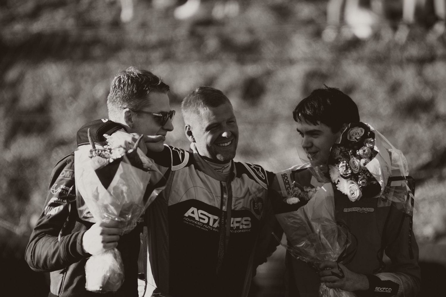 Black and white photo of three people celebrating with trophies at a racing event.