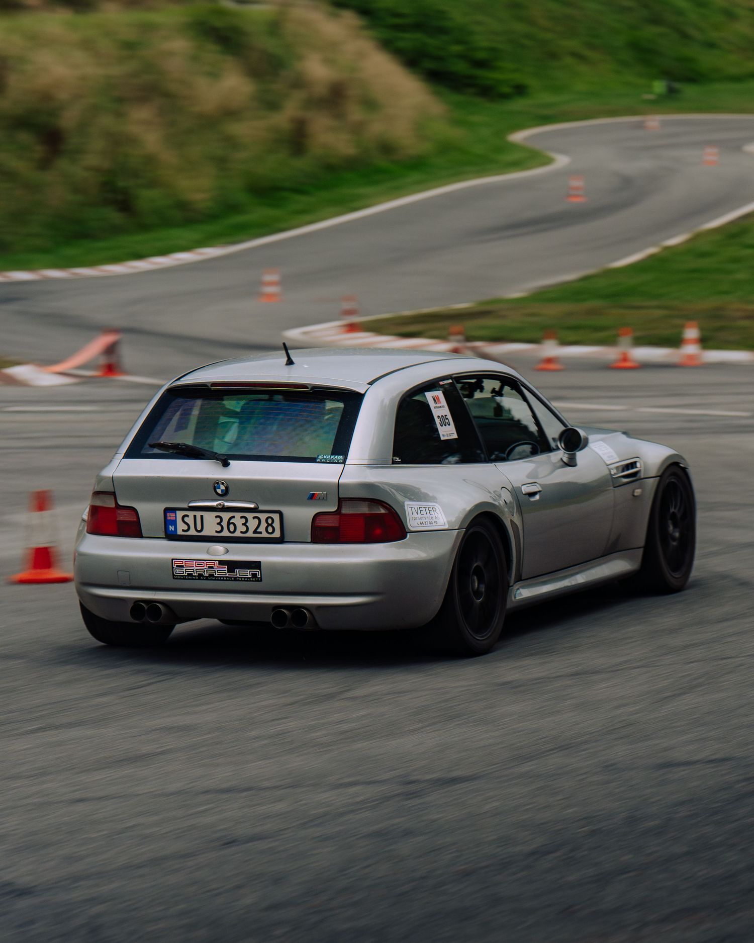 A silver sports car drifts through a cone course on a winding road during a performance driving event.