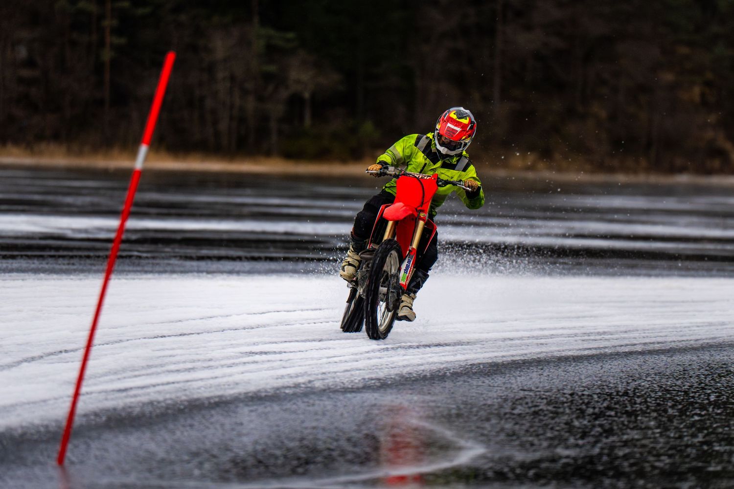 Ice skater gliding across a frozen lake with red poles marking the path on a winter day.