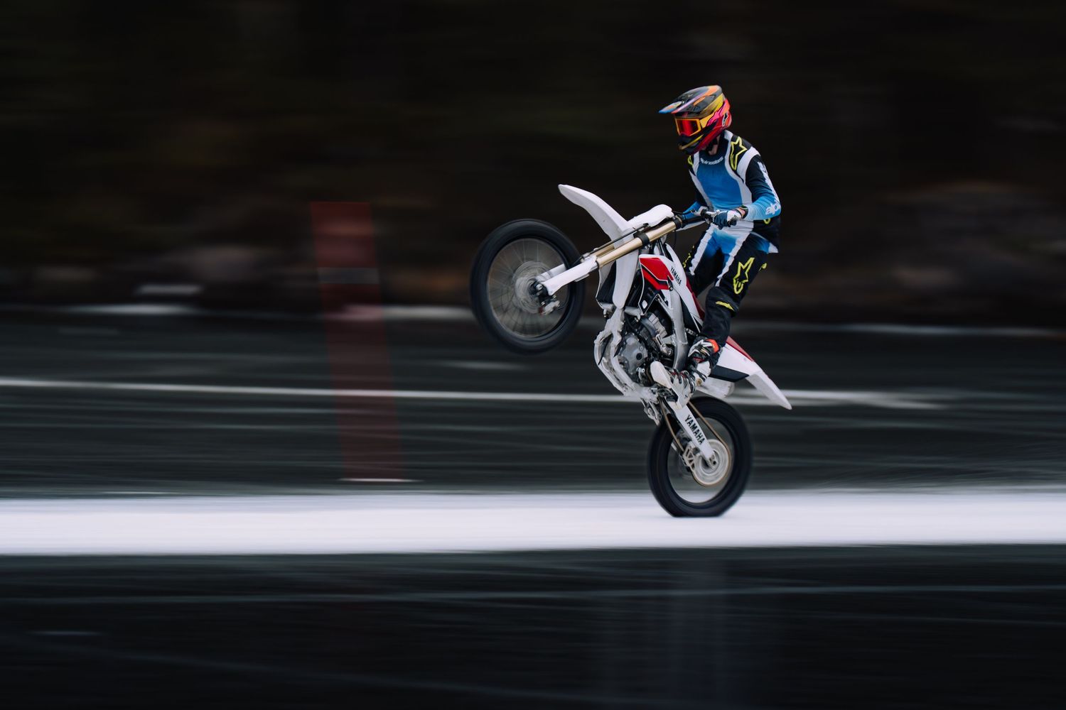 Motorcycle performing a wheelie stunt on dark asphalt with motion blur creating a dynamic speed effect.