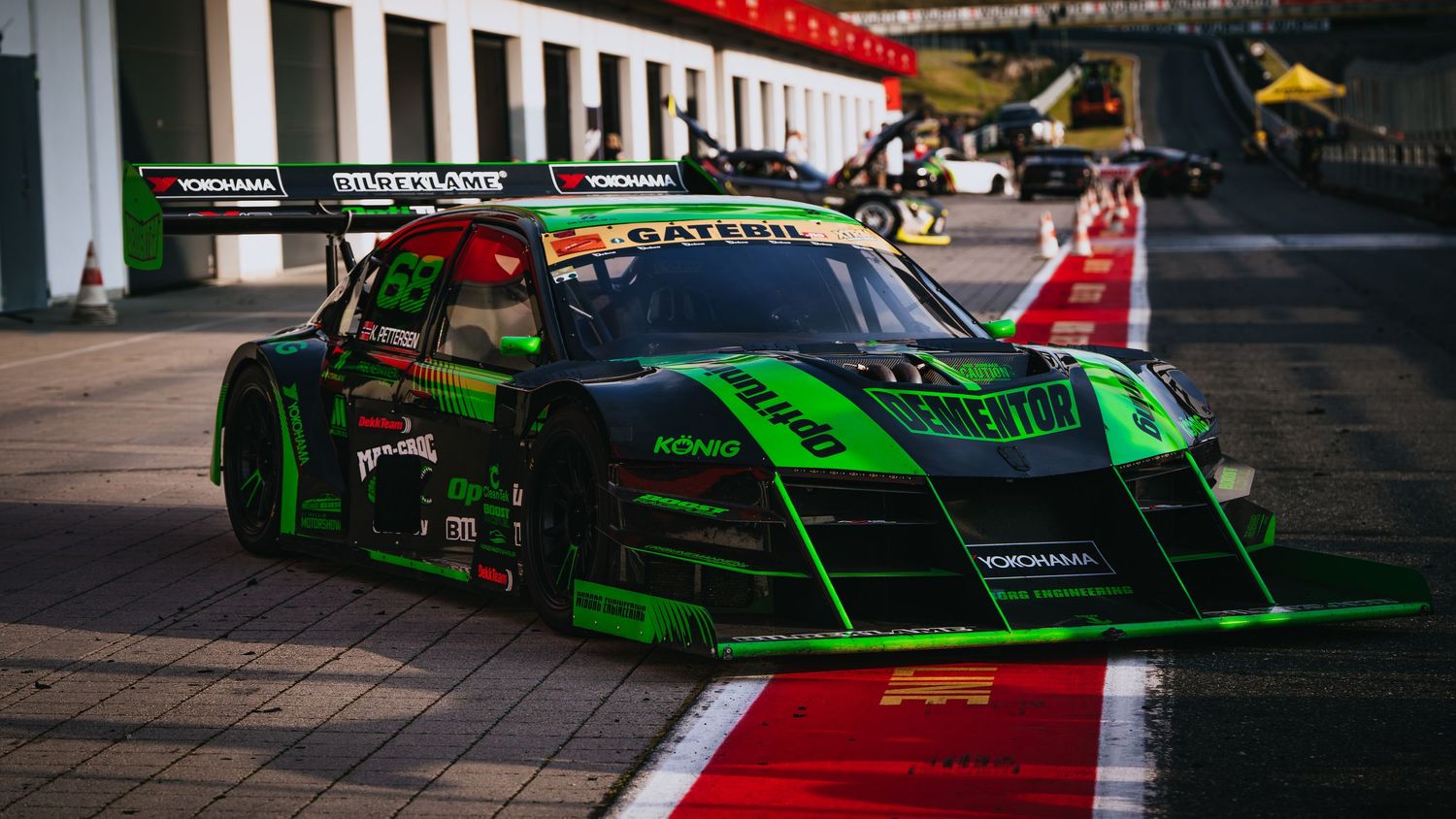 Multiple race cars lined up at a motorsport event with bright green and red liveries visible on track.