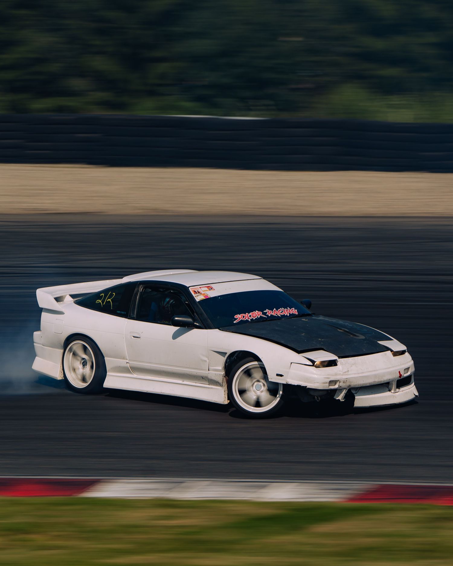 White Nissan Silvia S15 drifting on a racetrack with motion blur effect showing speed and precision.