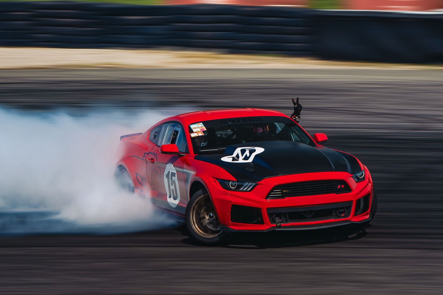 Red sports car drifting on a race track with tire smoke trailing behind it during a motorsport competition.
