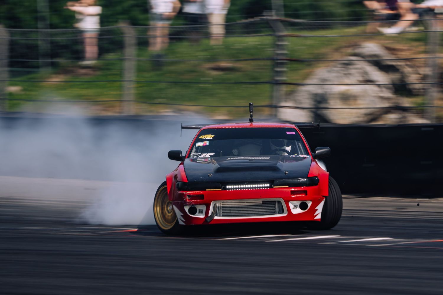 Red sports car drifting on race track with smoke trailing from tires during motorsport competition.