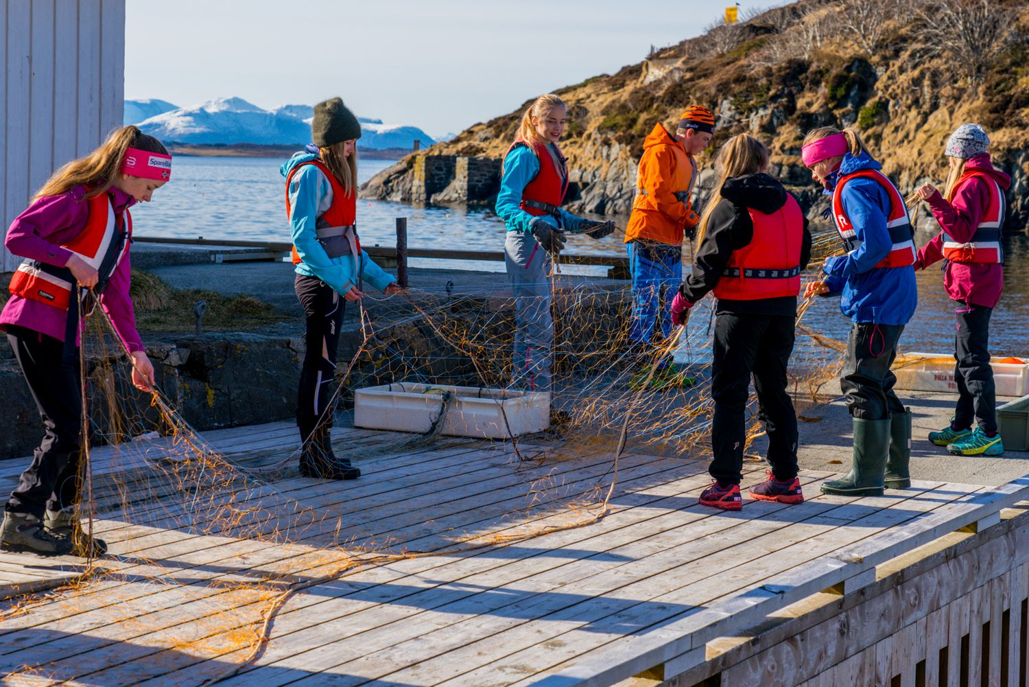 Group activity on snowy dock with mountains visible in background.