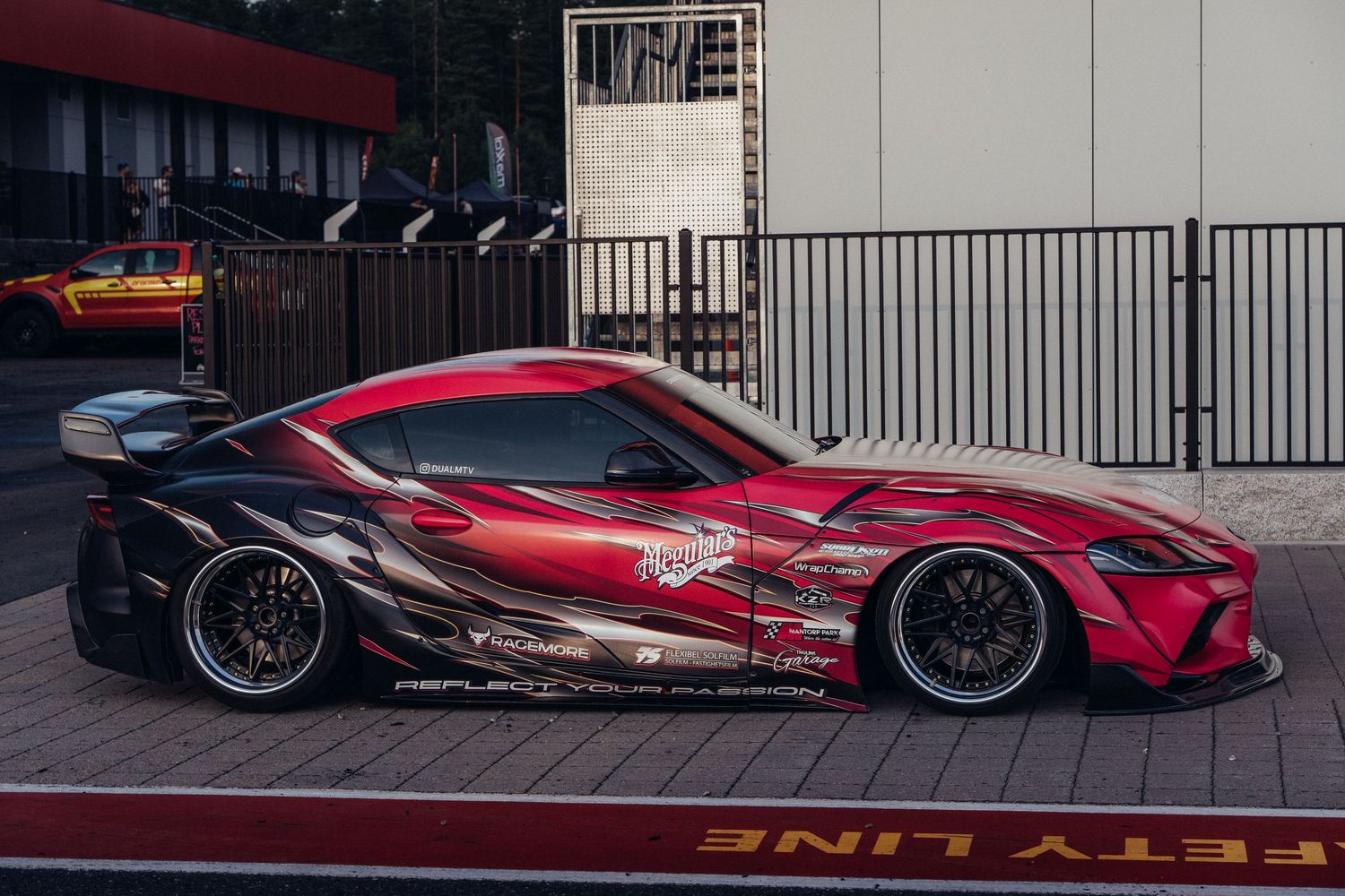 A modified red Toyota Supra with custom body kit, graphics and black wheels parked on a street.