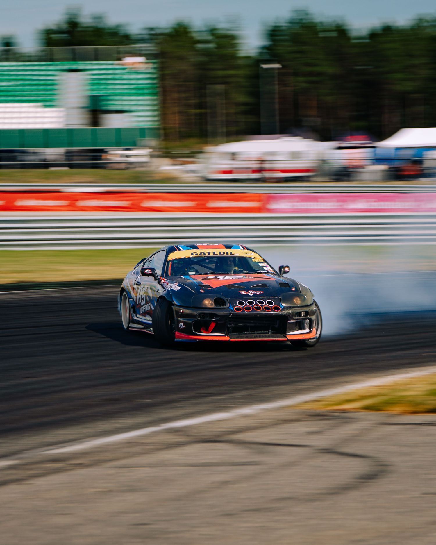 Multiple race cars drift in formation on a motorsport track during a competitive drifting event.