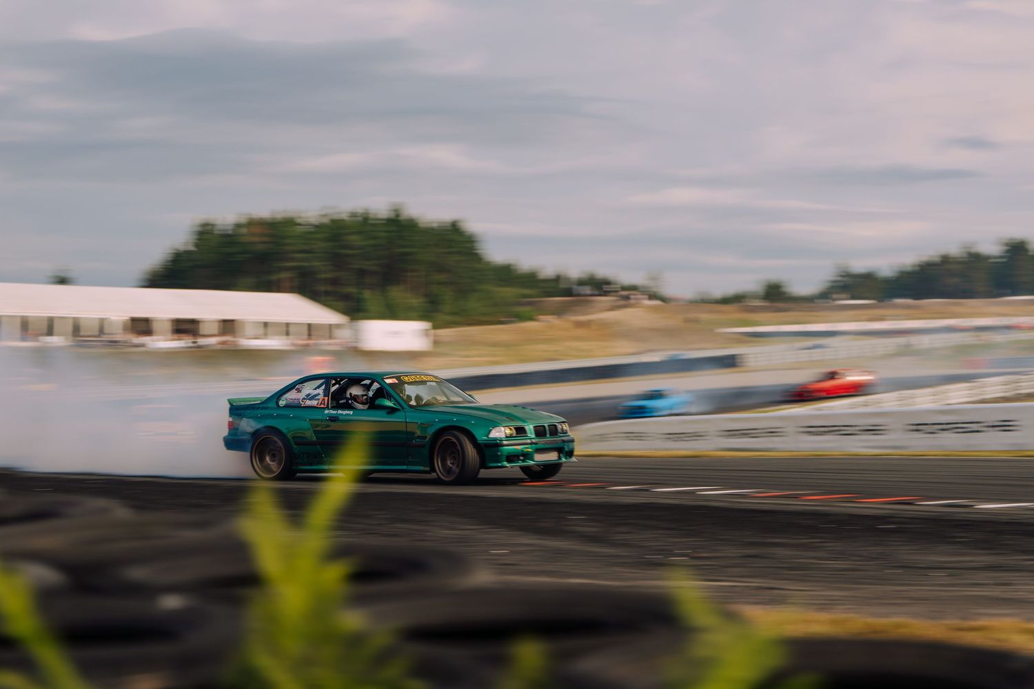 A green sports car drifting on a race track with motion blur against an overcast sky.