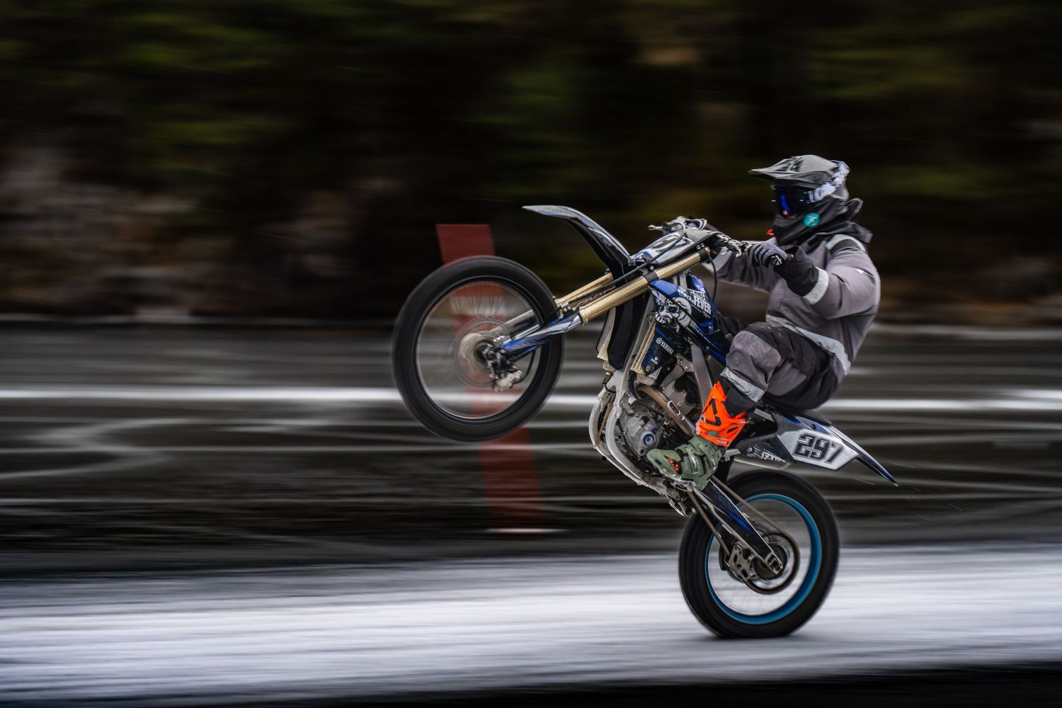 A motorcycle performing a high-speed wheelie stunt on a racetrack, captured in motion blur effect.