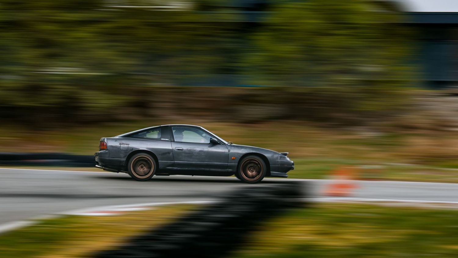 A silver sports car races through a winding mountain road with motion blur and scenic landscape views.