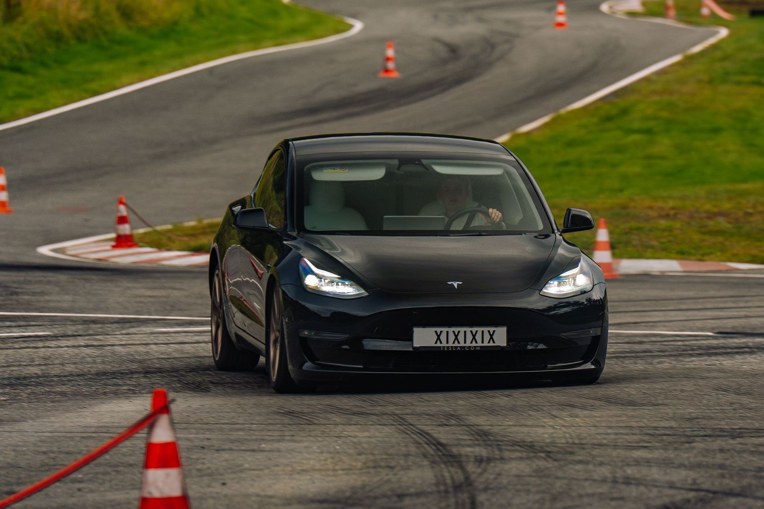 A black sports car navigates through orange traffic cones on a curving asphalt track during a driving event.