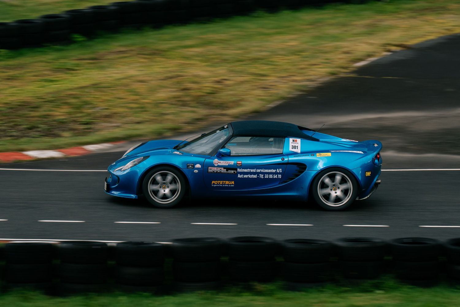 Blue sports car zooms around a curved racetrack with a scenic green landscape in the background.