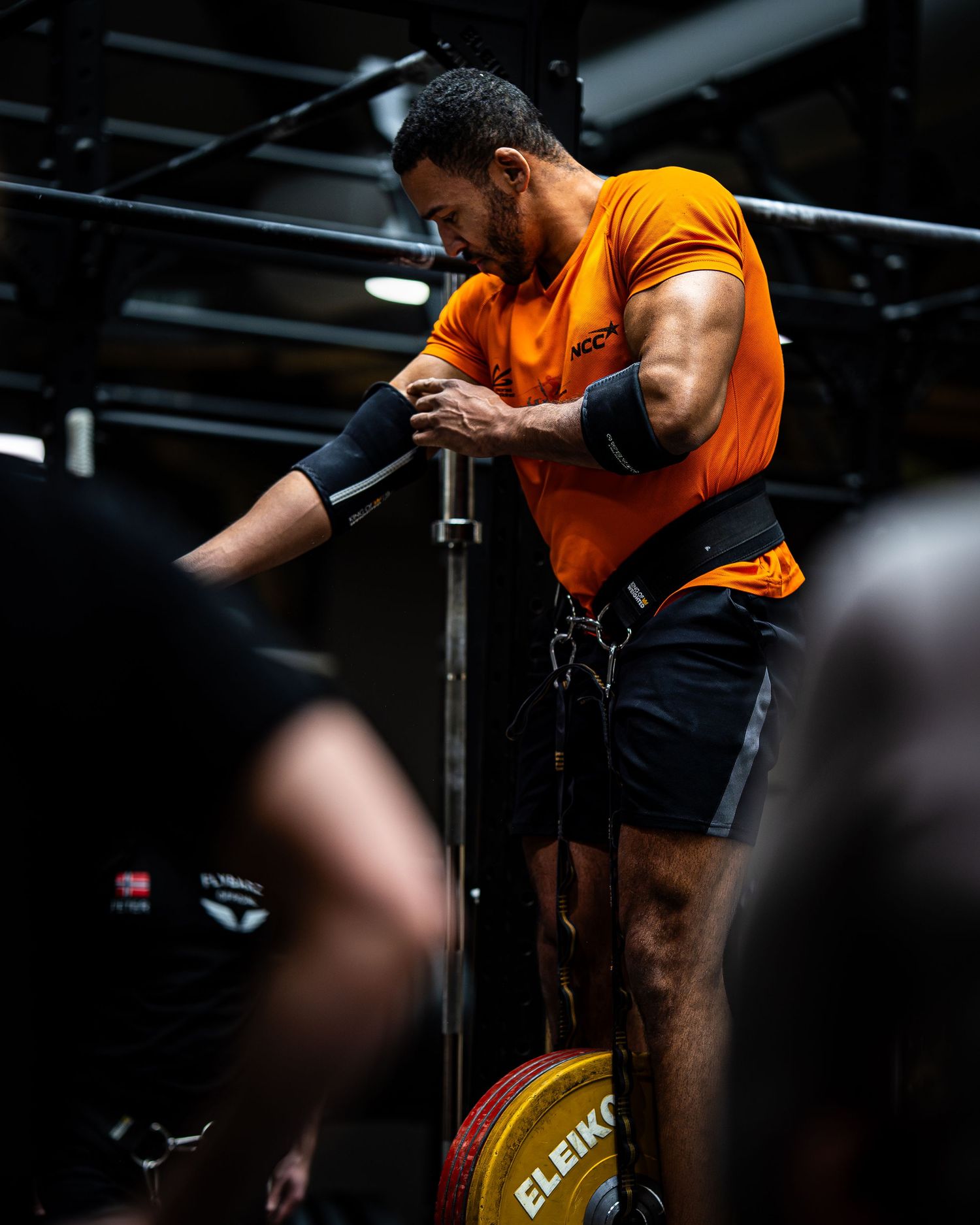 Person in orange shirt performing assisted dips exercise at CrossFit gym.