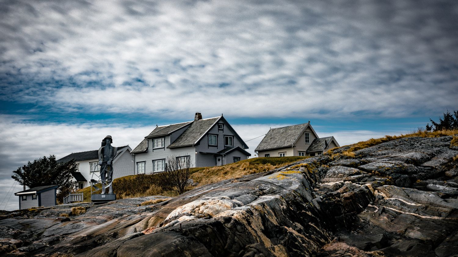 Weathered coastal homes perched on rocky cliff overlooking the sea under moody skies.