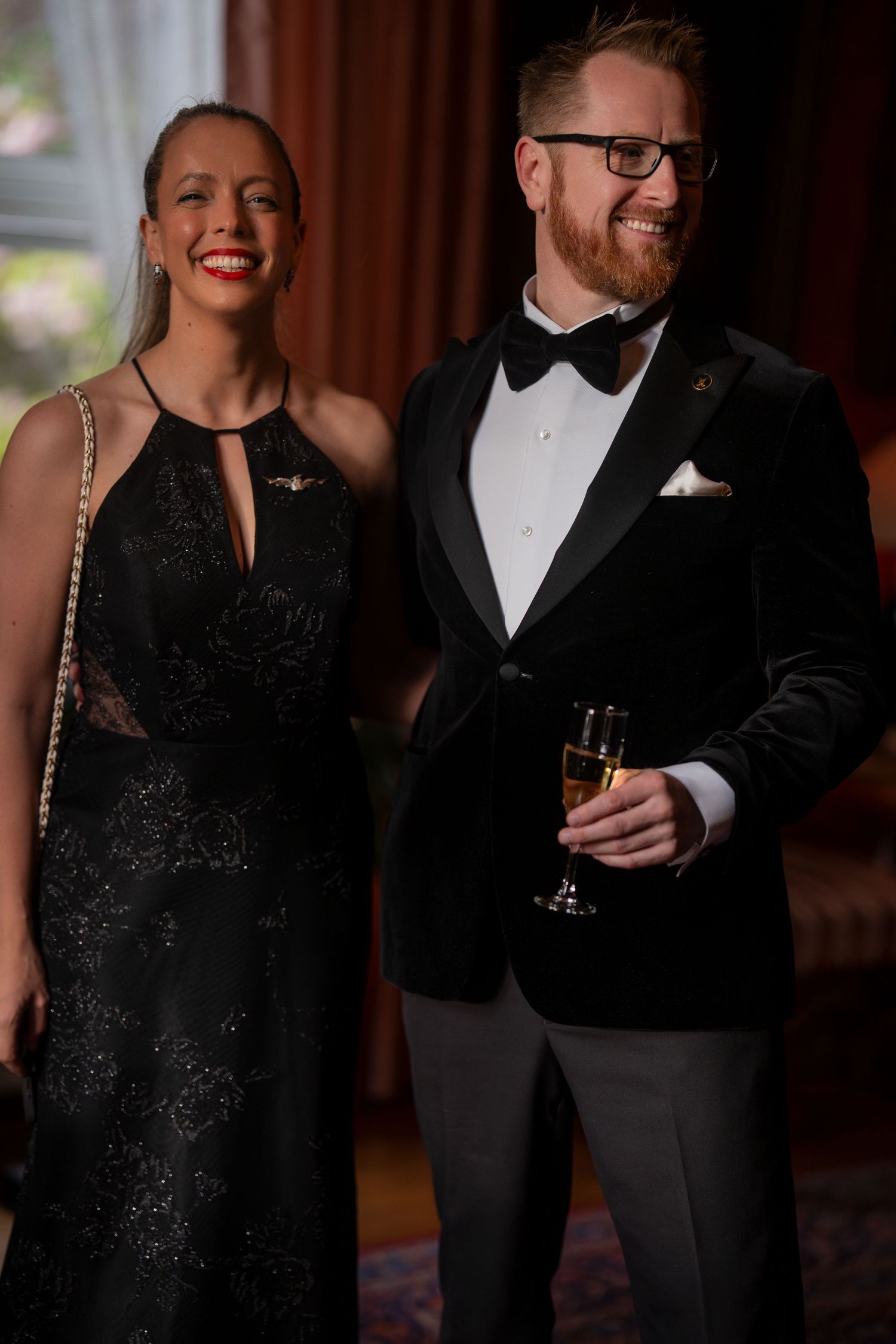 Elegant couple in formal attire sharing a moment at an upscale event with a black sparkly dress and tuxedo.