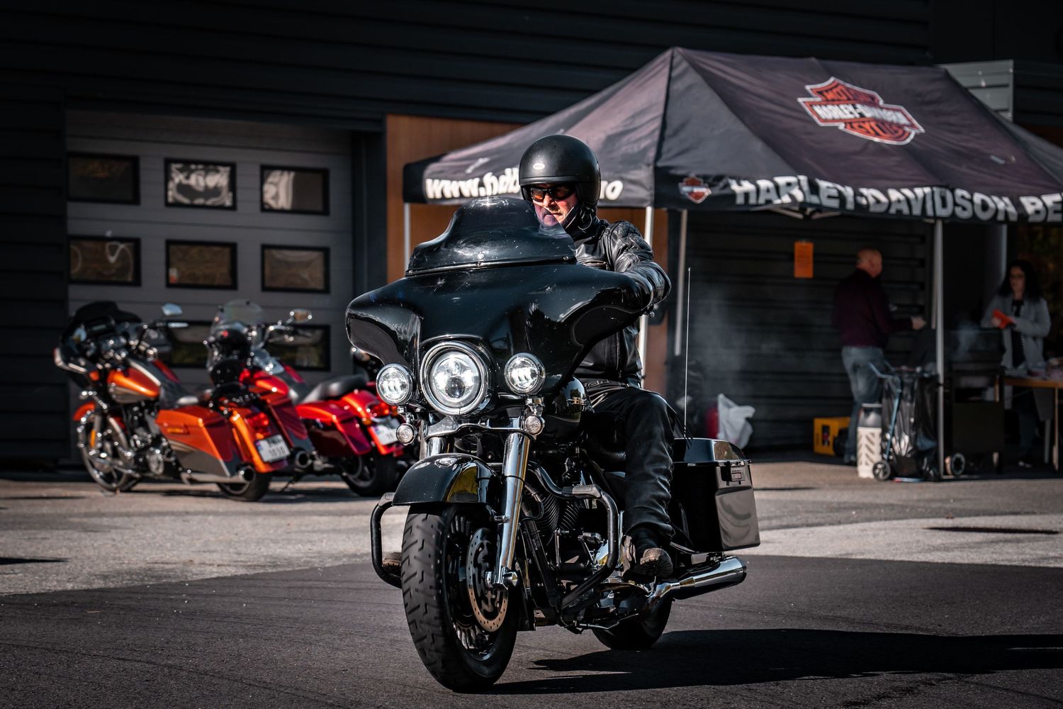 Harley-Davidson touring motorcycle parked under dealer tent with other bikes visible.