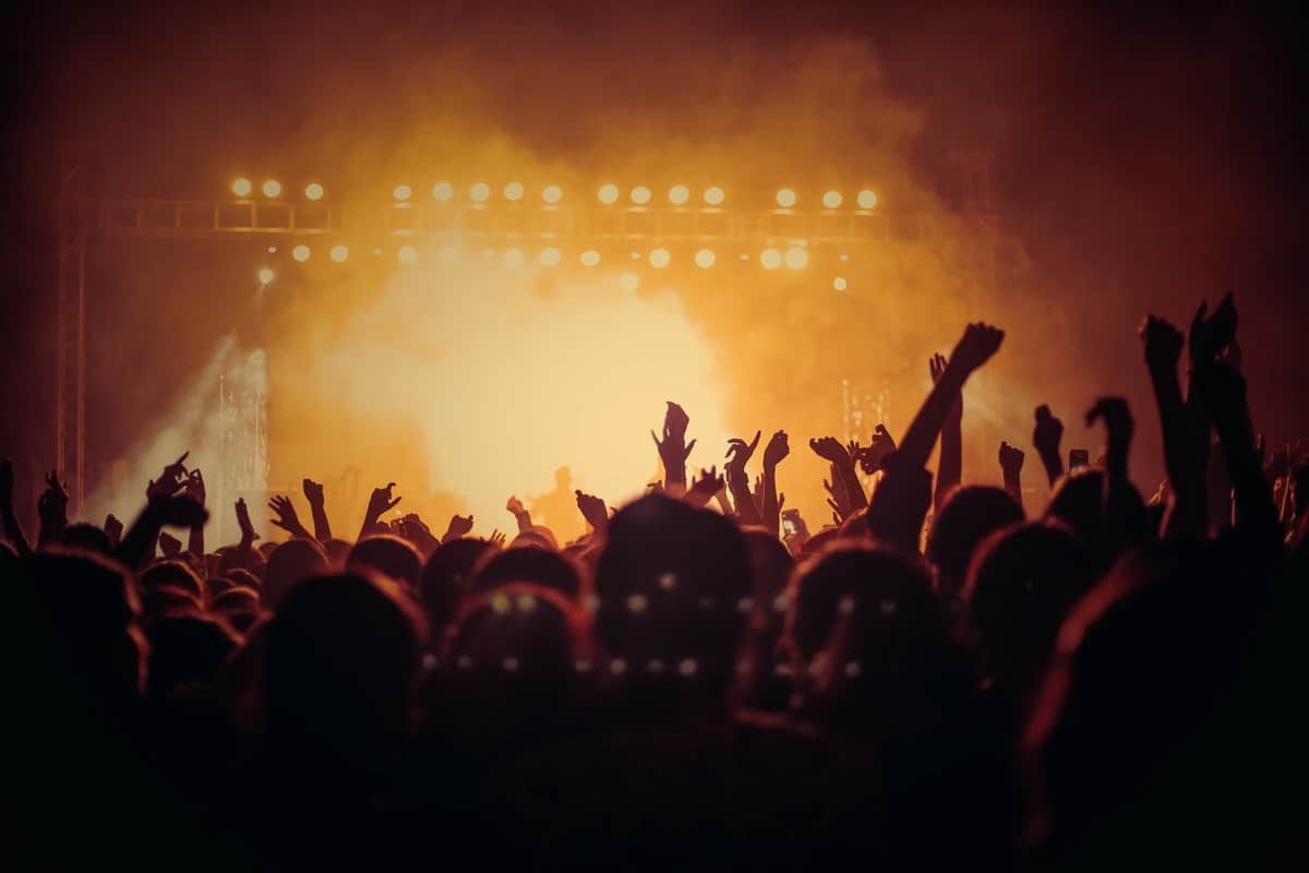 Silhouetted concert crowd with raised hands against orange stage lighting and smoke effects during live performance.