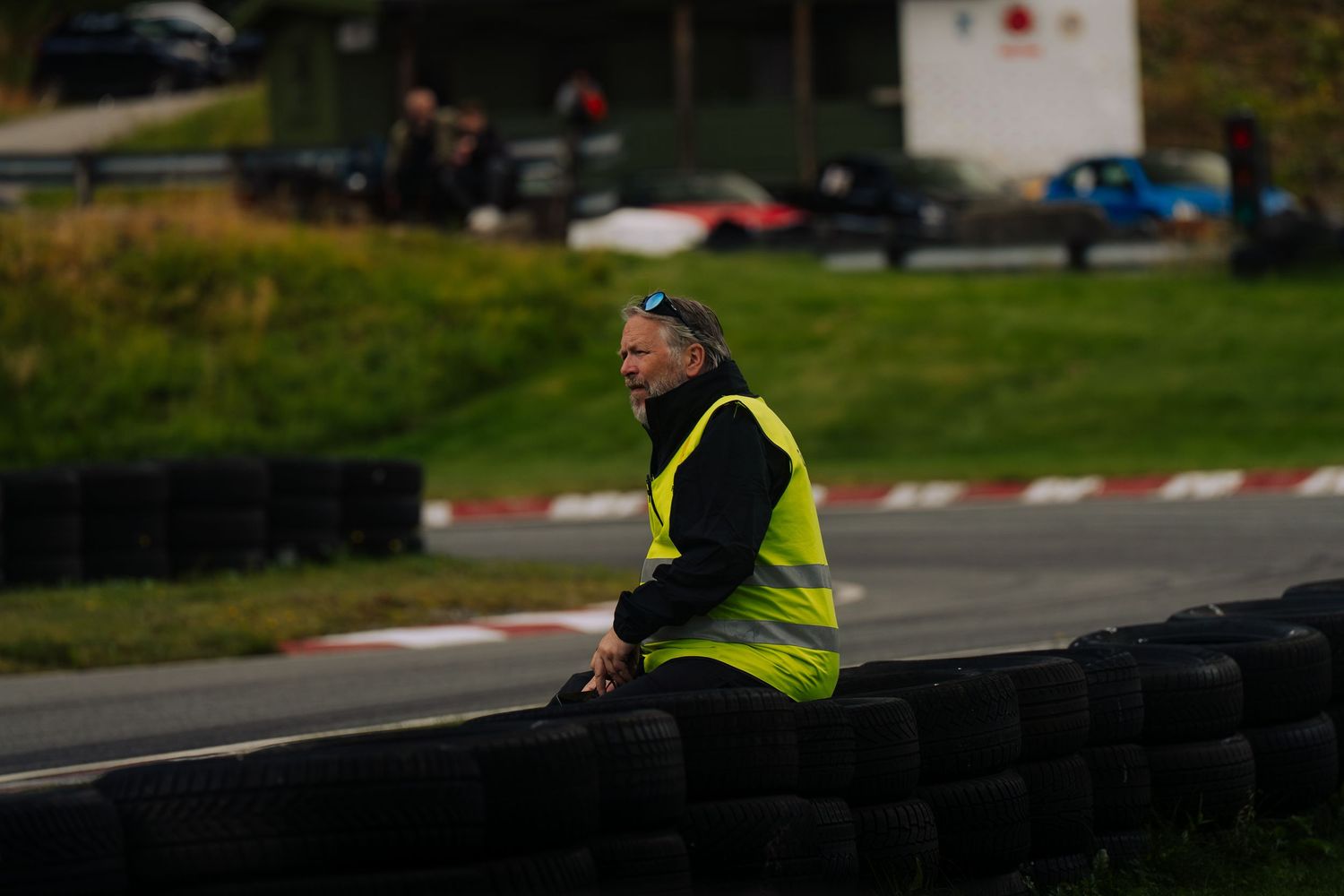 A person in a high-visibility safety vest stands near a race track during a motorsport event.