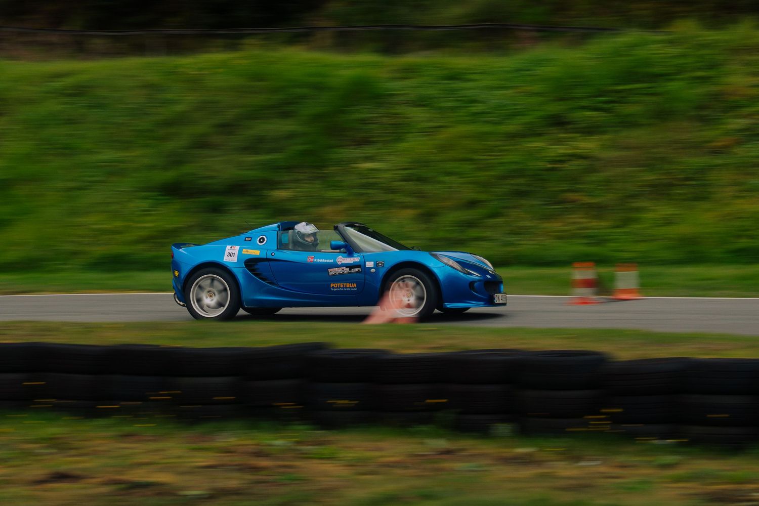 A bright blue sports car speeds along a racetrack with motion blur against a green background.