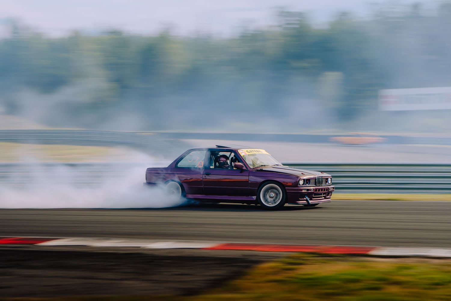A purple BMW drifting on a race track with smoke billowing from the tires during a drift competition.