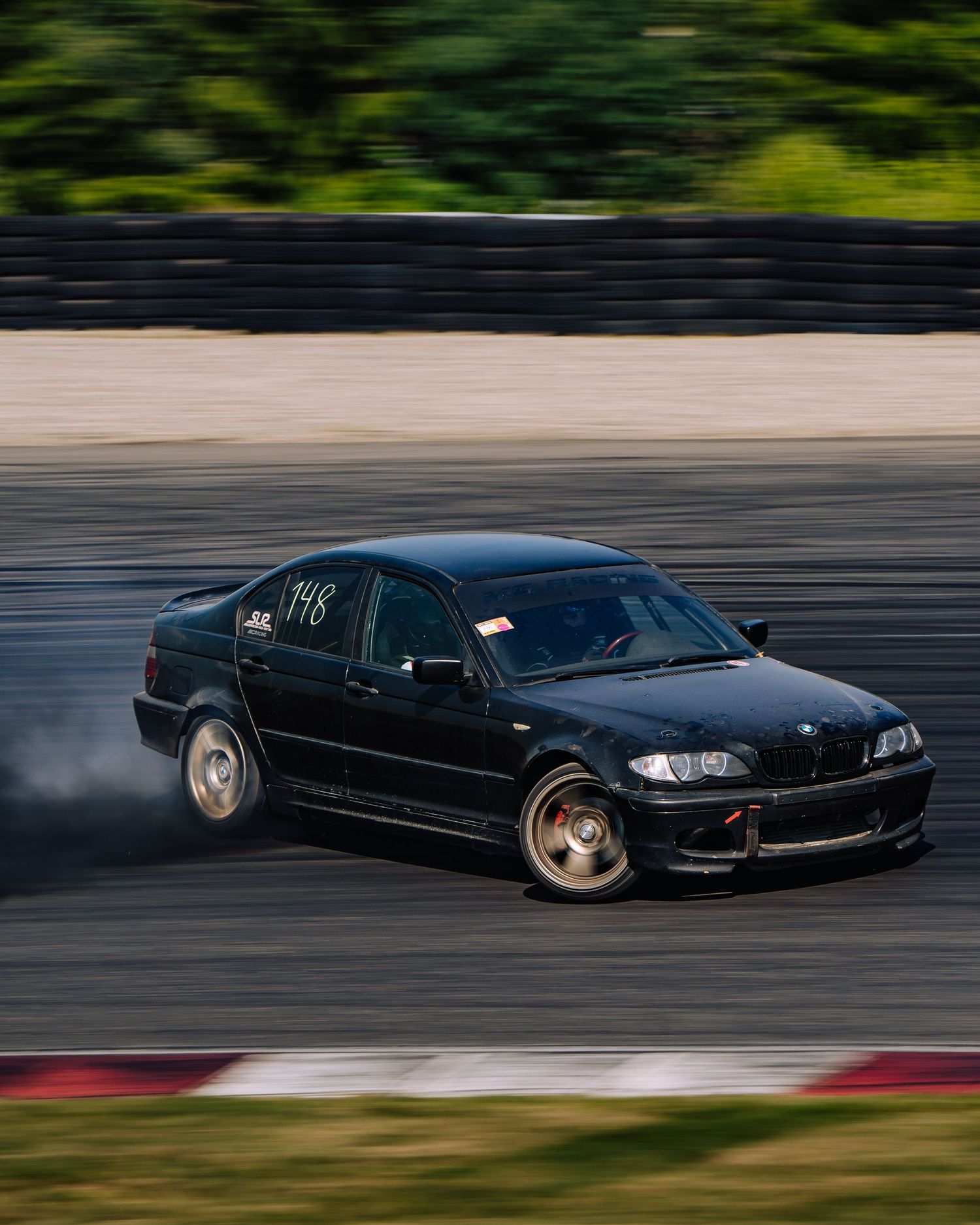 A black BMW drifting on a race track with motion blur, showing skilled performance driving technique.
