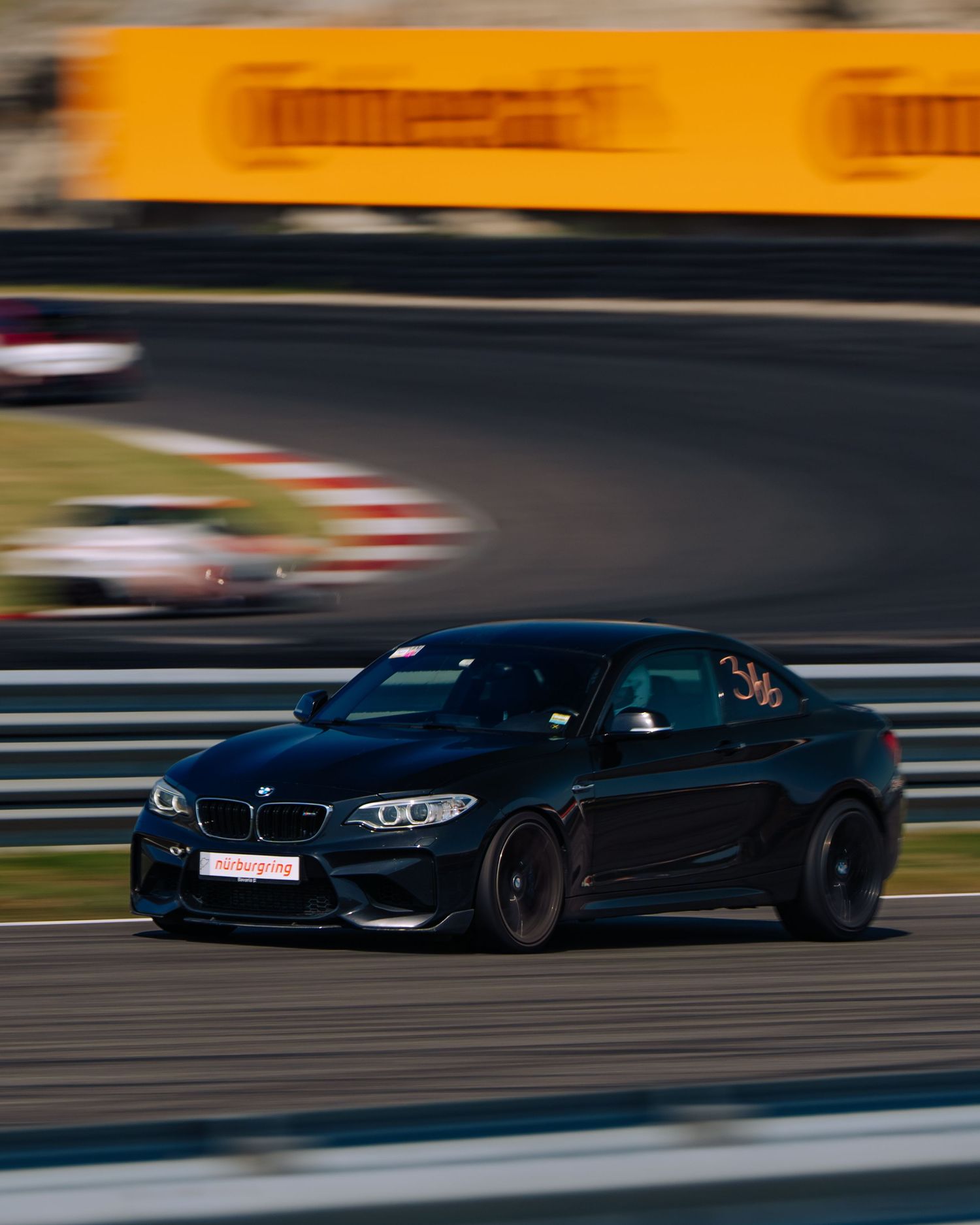 A sequence of dark BMW M4 sports cars racing on a track with motion blur and orange sunset lighting in background.