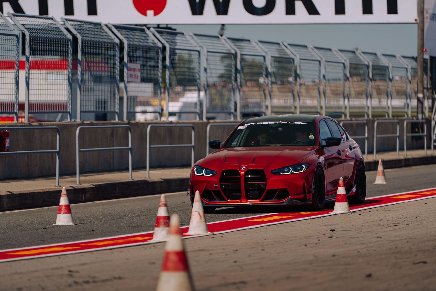 Red BMW M4 sports car on a racetrack with safety cones and barriers at Fort Worth Motor Speedway.