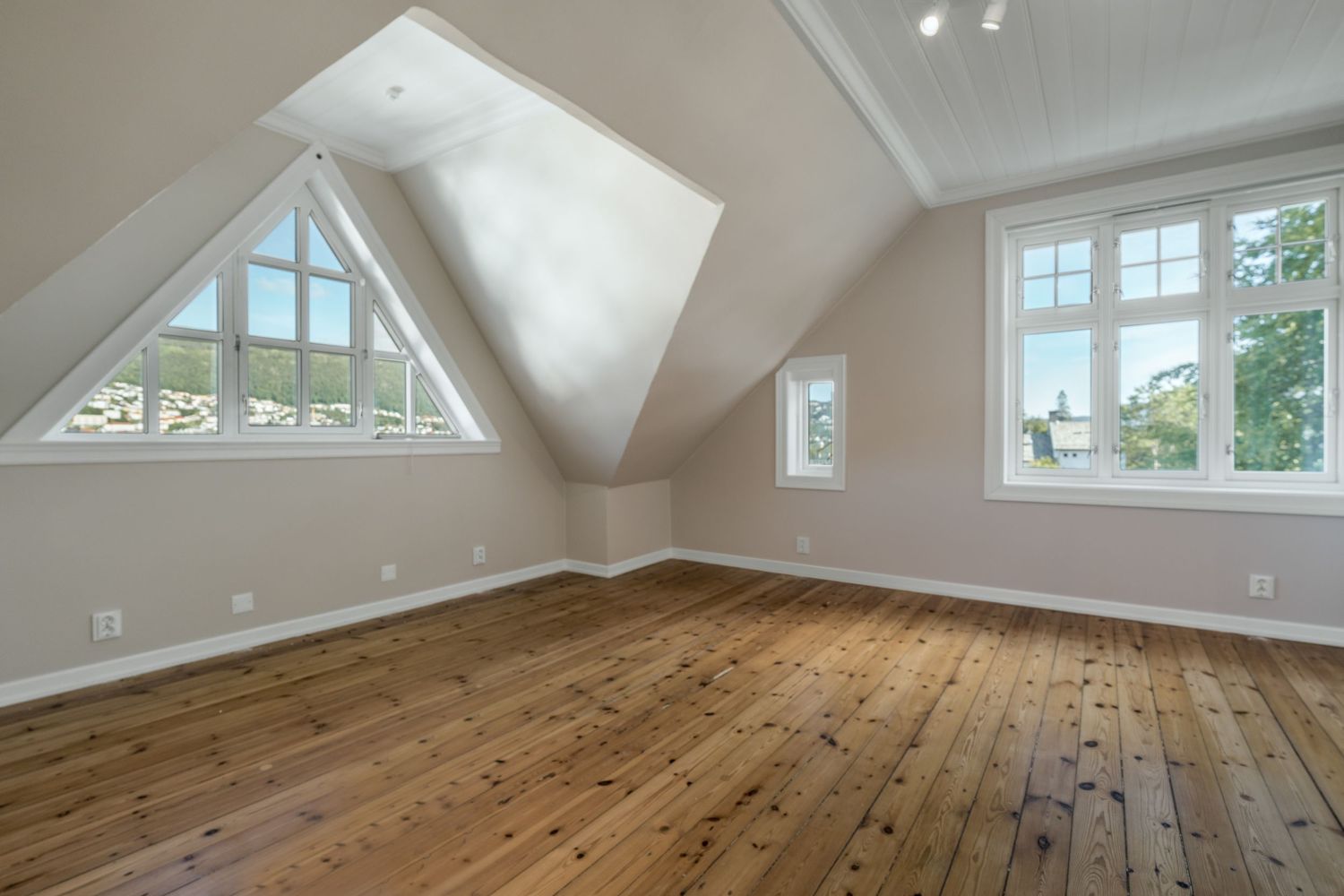 Attic room with vaulted ceiling, triangular windows, and warm wood flooring throughout.