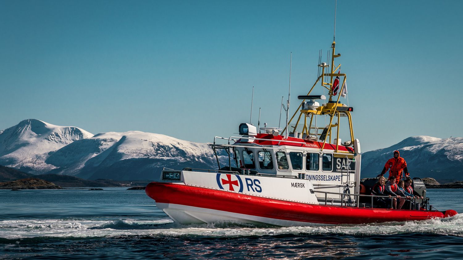 Red rescue boat cruising through icy waters with snow-covered mountains in distance.