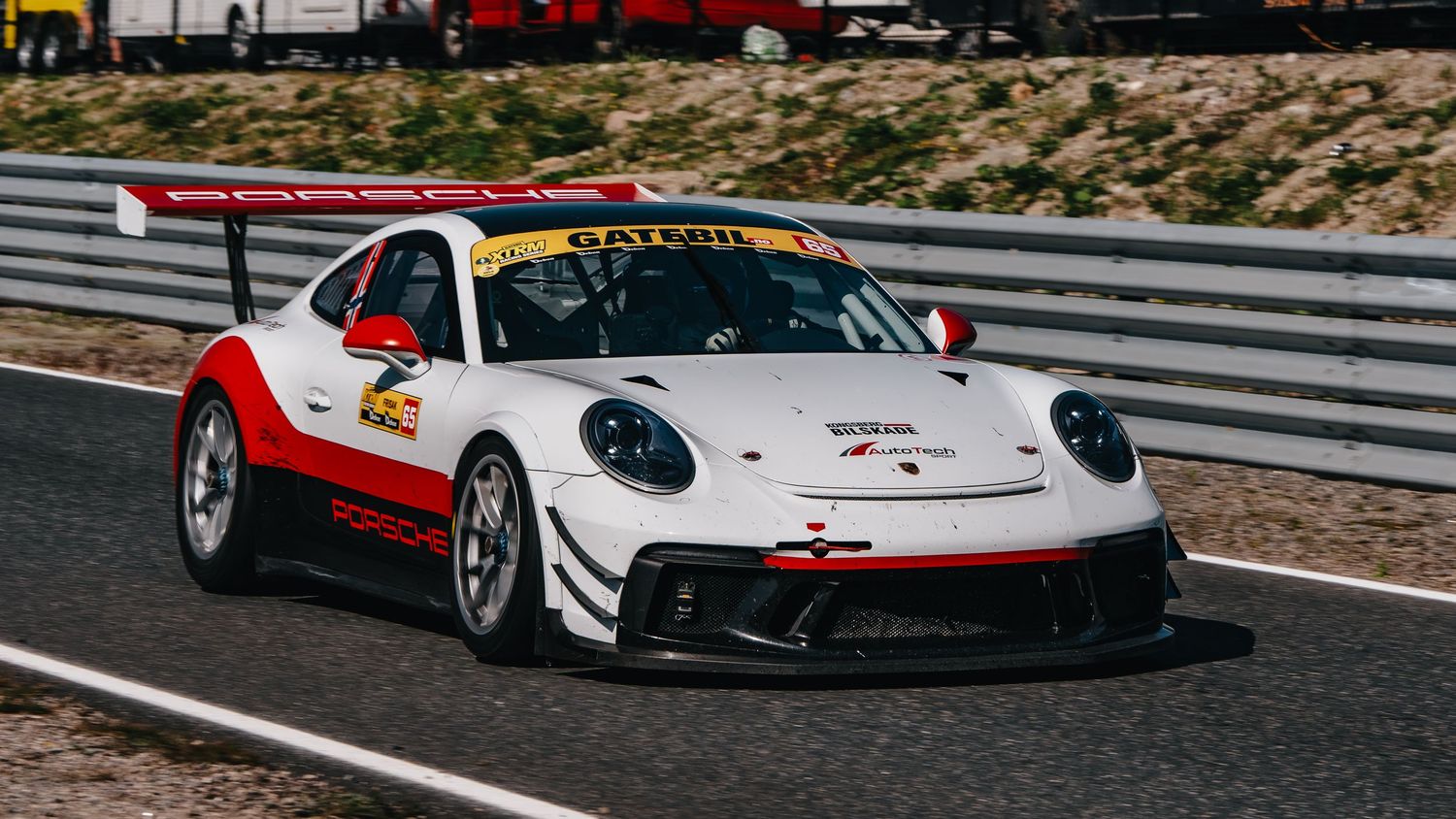 Red and white Porsche race car speeds around a racetrack during a motorsport competition.