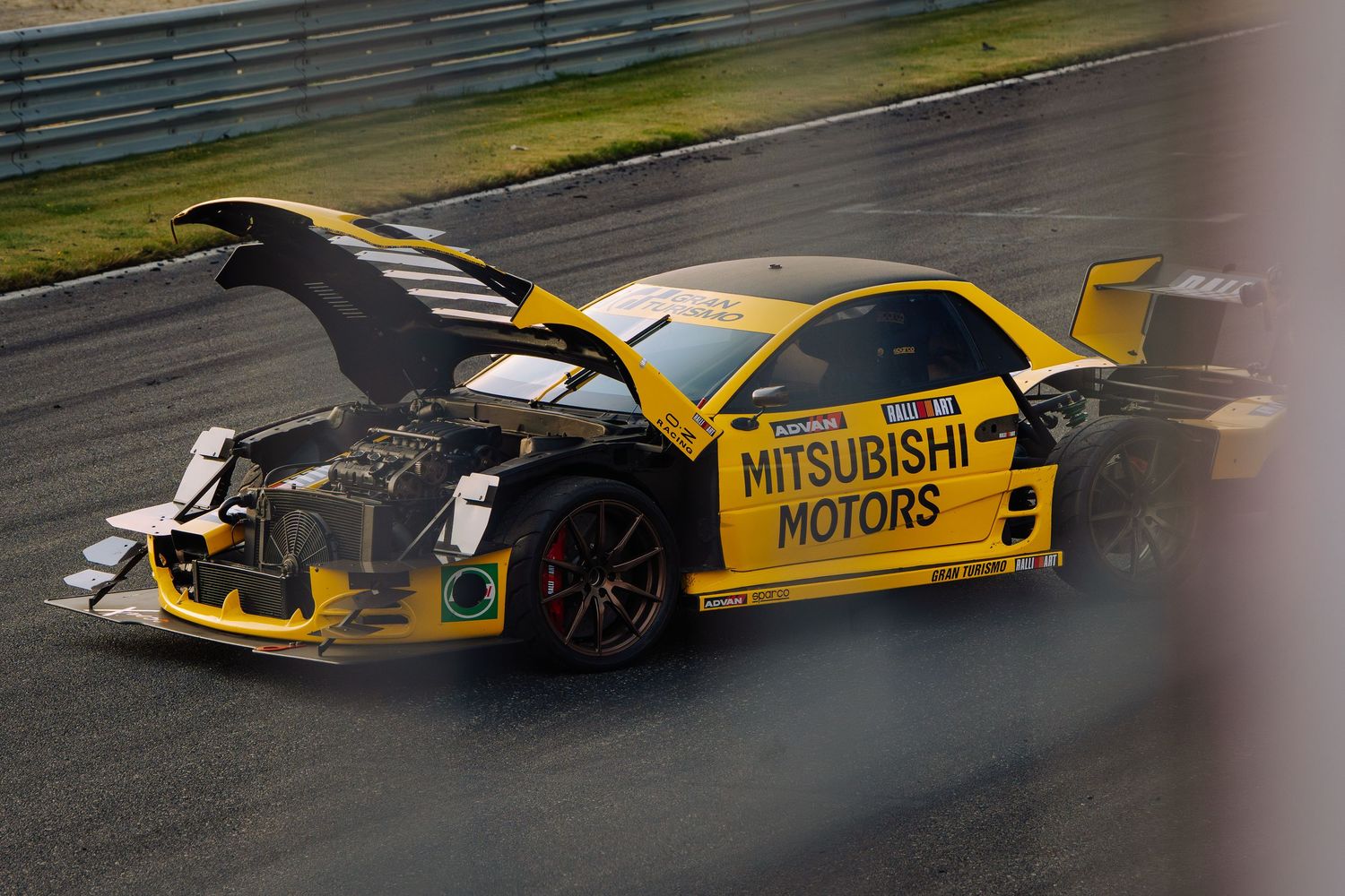 Yellow race car crashes and spins out on wet racetrack during high-speed motorsport competition.