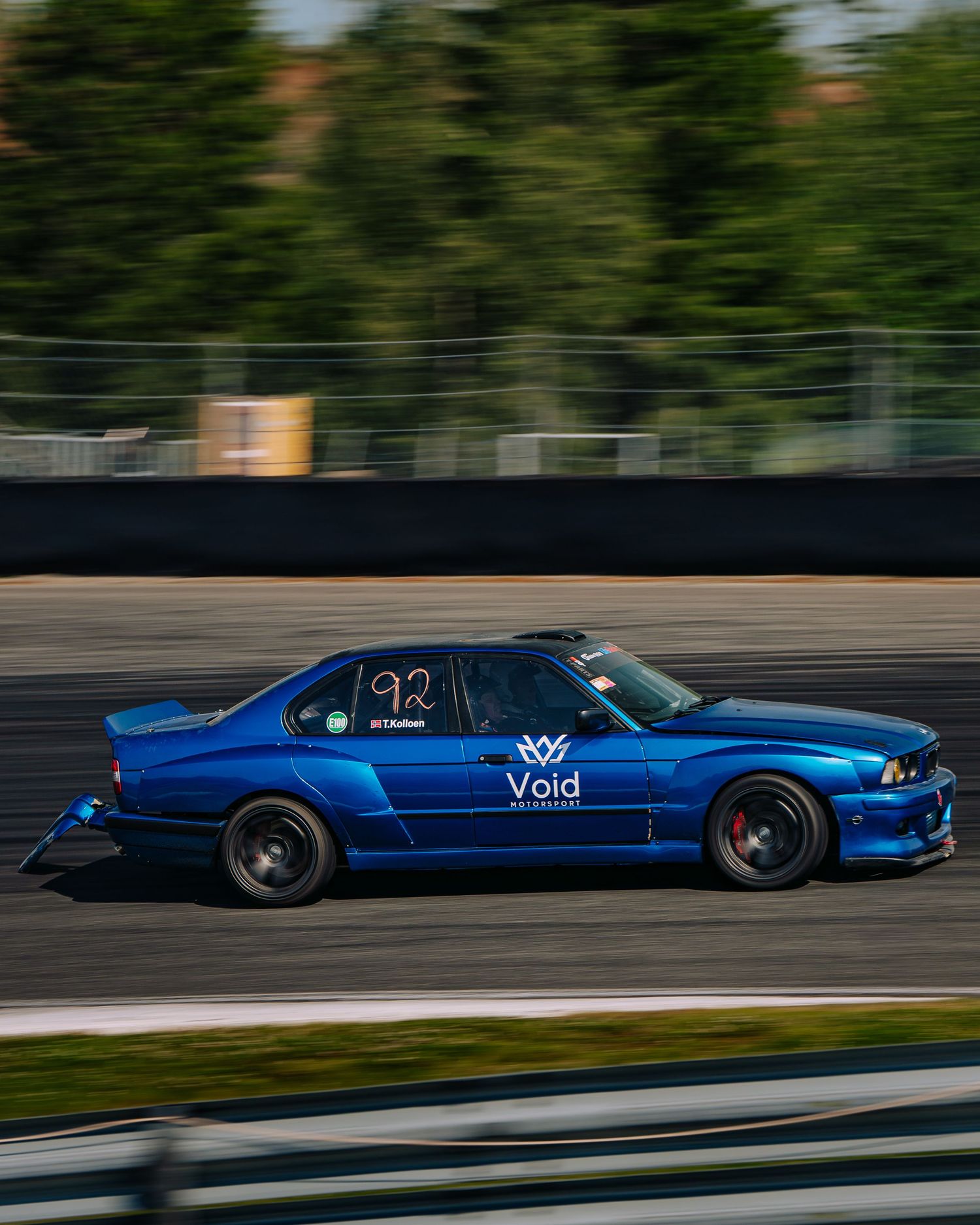 Blue sports car racing on a track with motion blur effect showing high-speed movement on a sunny day.