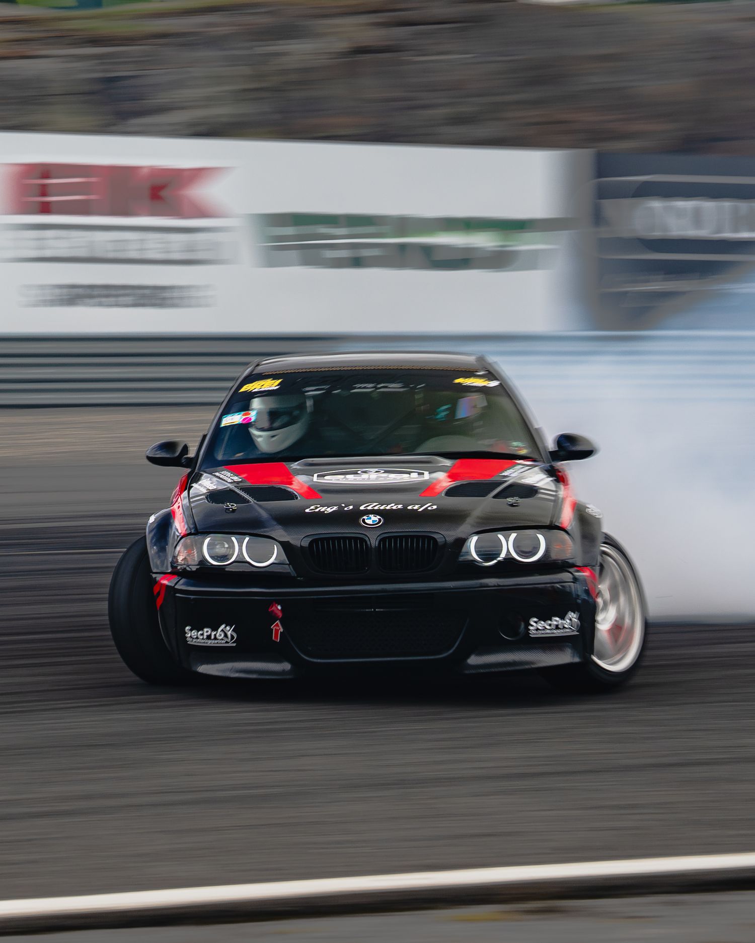 A black BMW M3 drifts on a track with smoke billowing from its tires during a motorsport event.